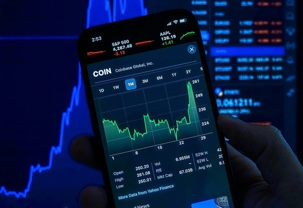 a close up of someone holding their phone and on the screen is the coinbase ipo stock chart, a stock chart is also in the background which is blue